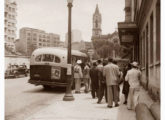 Ônibus Grassi embarca fila de passageiros em ponto final junto ao Largo do Paissandú, São Paulo (SP); ao fundo, Igreja de Nossa Senhora do Rosário dos Pretos.